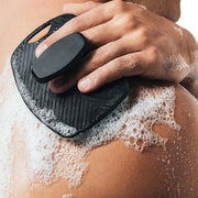 Người dùng cầm miếng bọt biển đen tạo bọt xà phòng trên lưng, bọt trắng nổi bật.