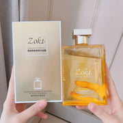 Chai sữa tắm Zokt, màu vàng nhạt, nắp bạc, đặt cạnh hộp giấy thiết kế thanh lịch.