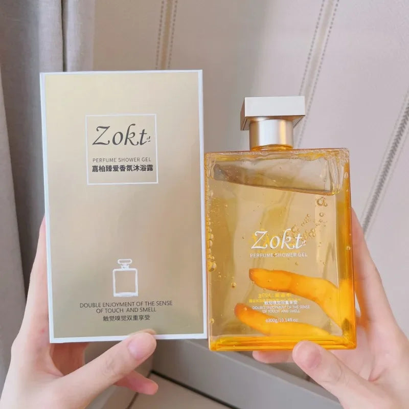 Chai sữa tắm Zokt, màu vàng nhạt, nắp bạc, đặt cạnh hộp giấy thiết kế thanh lịch.