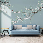 Sofa xanh, gối xám, tường màu xanh nước biển, hoa trắng, chim và bướm trang trí.