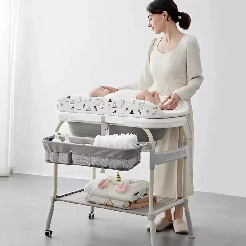 Người phụ nữ chăm sóc em bé trên bàn thay tã màu trắng có họa tiết, bên dưới có giỏ đựng đồ.