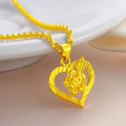 Dây chuyền vàng với mặt hình trái tim và hoa nổi, đặt trên nền màu hồng nhạt.