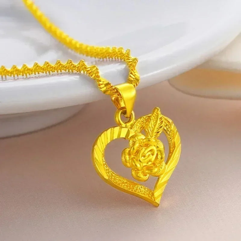 Dây chuyền vàng với mặt hình trái tim và hoa nổi, đặt trên nền màu hồng nhạt.