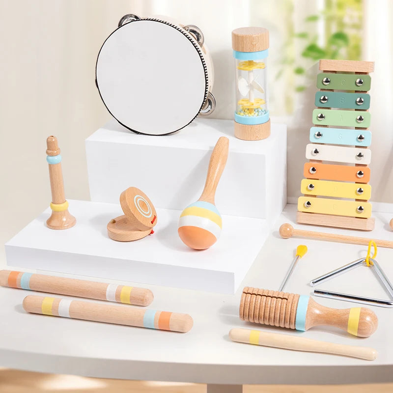 Bộ nhạc cụ đồ chơi gỗ với màu pastel gồm trống lắc, đàn phiến, và thanh gõ trên nền trắng.