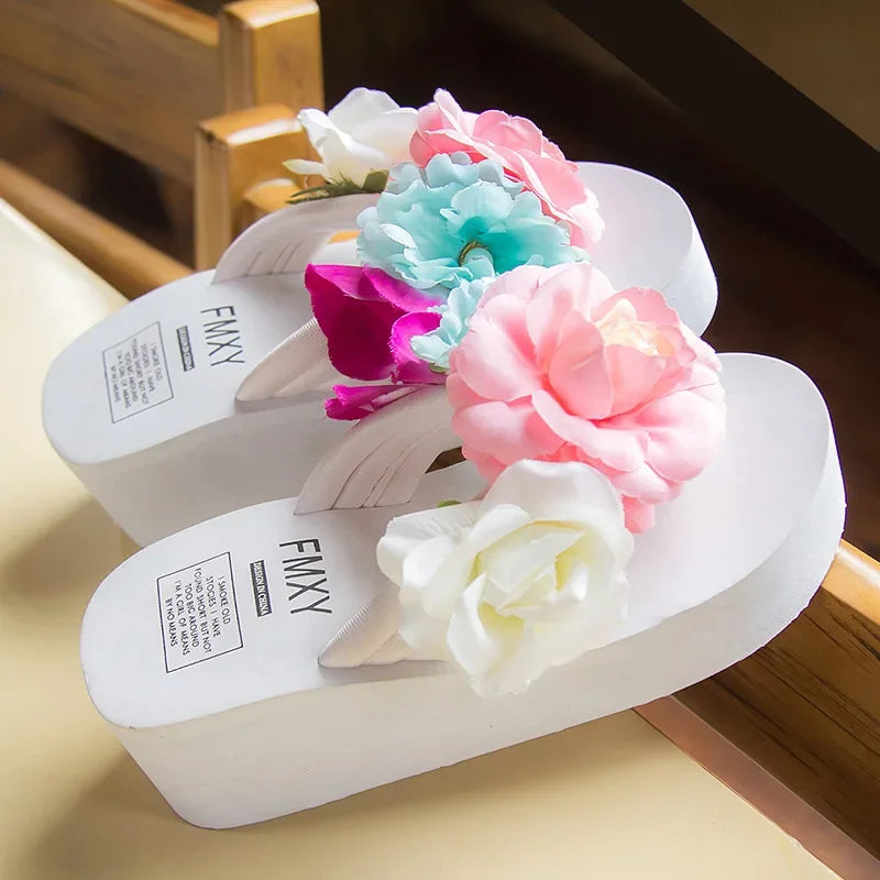 Dép đế cao màu trắng trang trí hoa giả nhiều màu sắc như hồng, xanh và trắng.