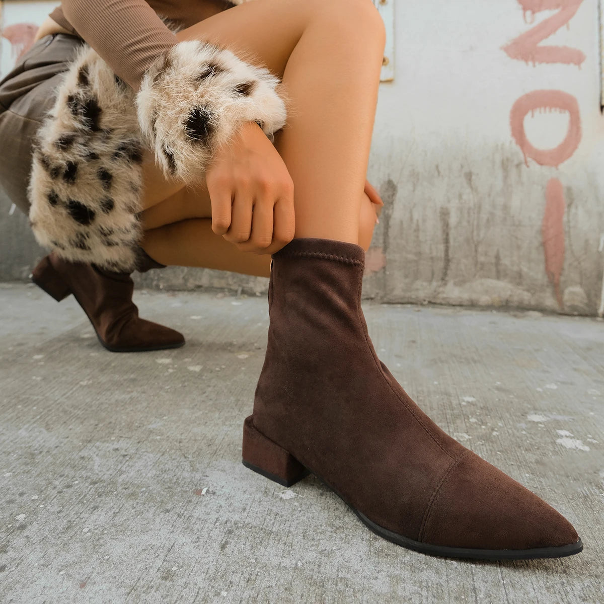 Người mặc boot nâu, váy lông vằn đen trắng, ngồi trên nền bê tông xám.
