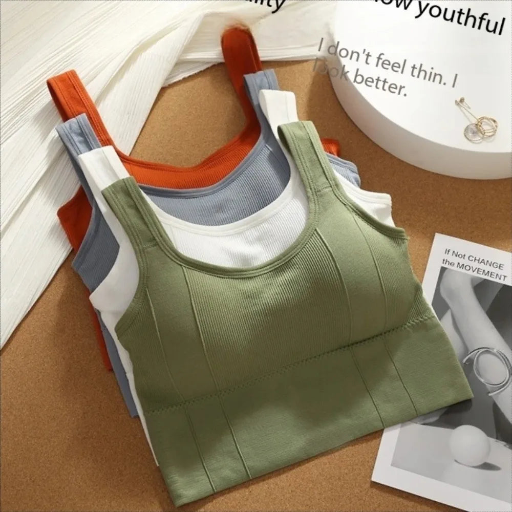 Bộ ba áo tank top xếp chồng: màu xanh lá, xám và cam, trên nền bàn gỗ sáng.