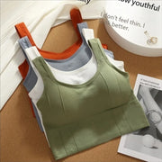 Bộ ba áo tank top xếp chồng: màu xanh lá, xám và cam, trên nền bàn gỗ sáng.