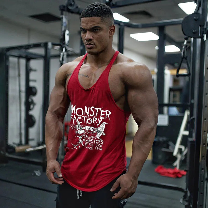 Người đàn ông cơ bắp mặc áo ba lỗ đỏ có chữ trắng, đứng trong phòng tập gym.
