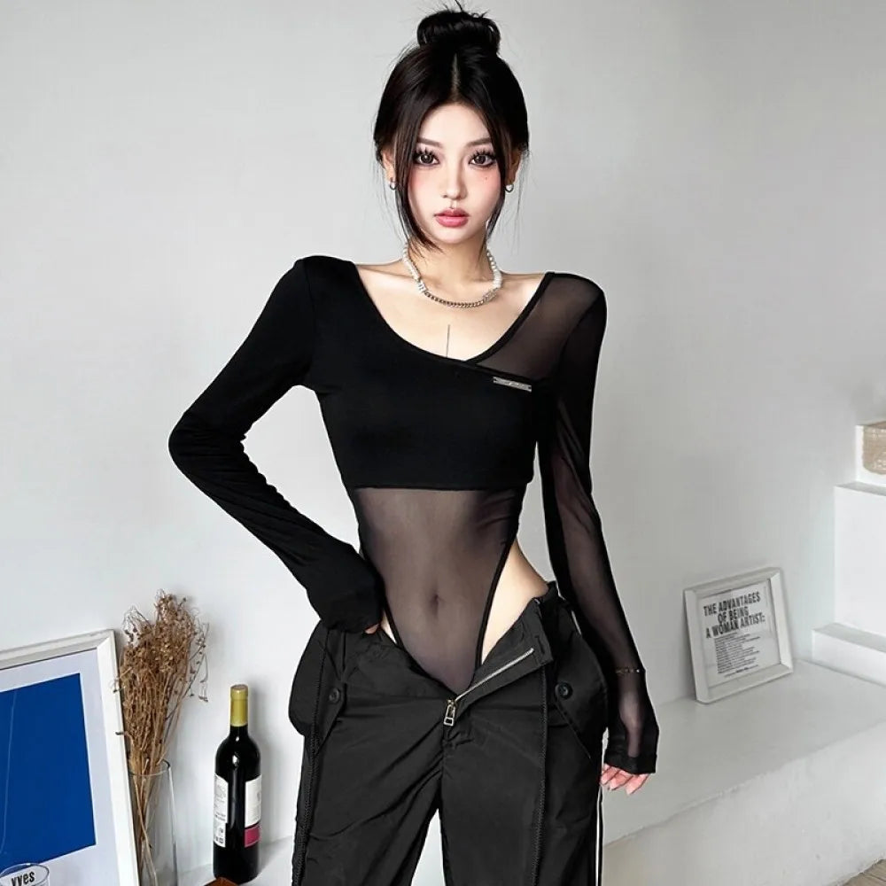 Người mẫu mặc áo đen xuyên thấu và quần đen, tóc búi cao, nền trắng.