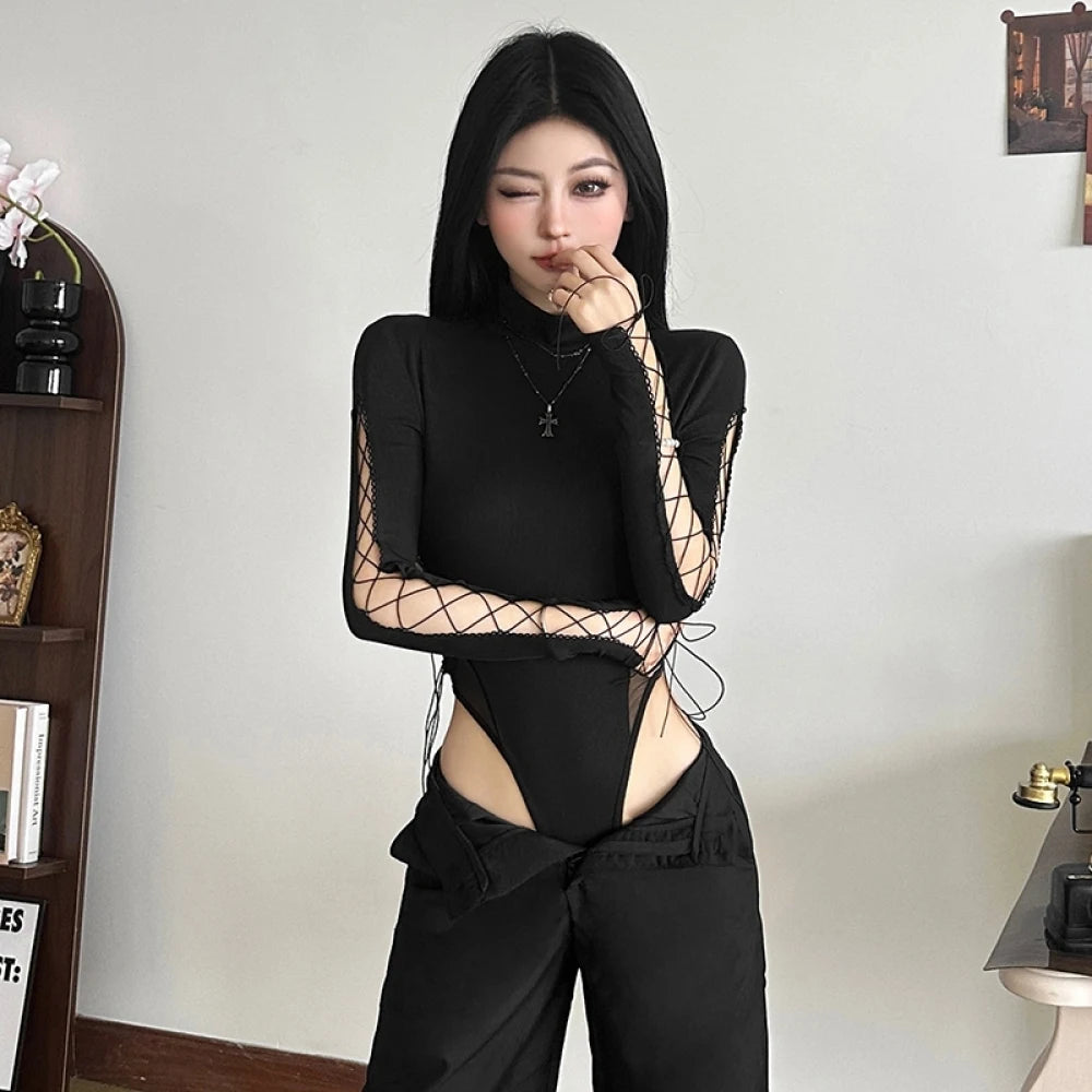 Người mặc áo đen dài tay lưới, tóc đen, đứng trong phòng, biểu cảm nháy mắt tinh nghịch.