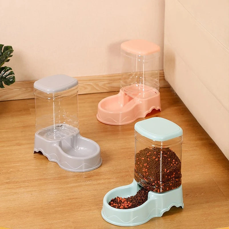 Ba máy đựng thức ăn cho thú cưng, màu xám, hồng và xanh, đặt trên sàn gỗ.