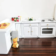 Nhà bếp đồ chơi màu trắng, chú chó nhỏ, thớt cam, lọ gia vị, rau trong bồn rửa, sàn gỗ nâu.