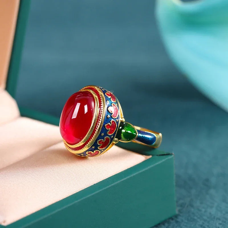 Nhẫn đá đỏ với họa tiết hoa văn màu xanh, vàng, đỏ, đặt trong hộp đệm màu xanh lục nhạt.