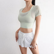 Người mặc áo tập màu xanh nhạt và quần ngắn trắng, đứng trước tường sáng.