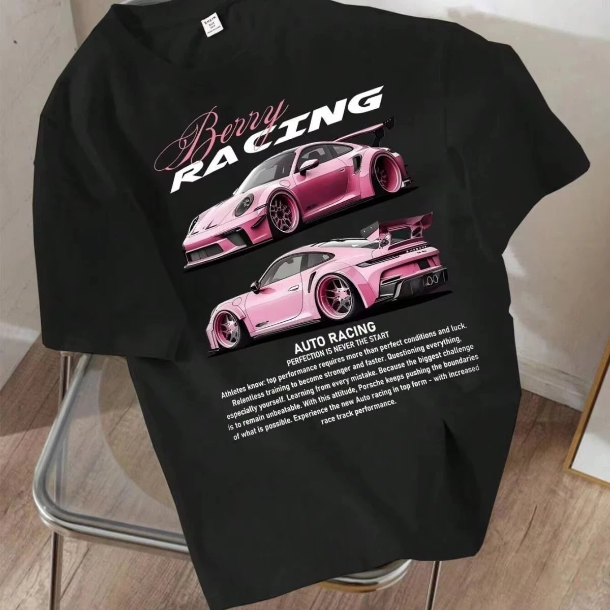 Áo thun đen in hình hai xe đua màu hồng, dòng chữ "Berry Racing", đặt trên ghế kim loại.