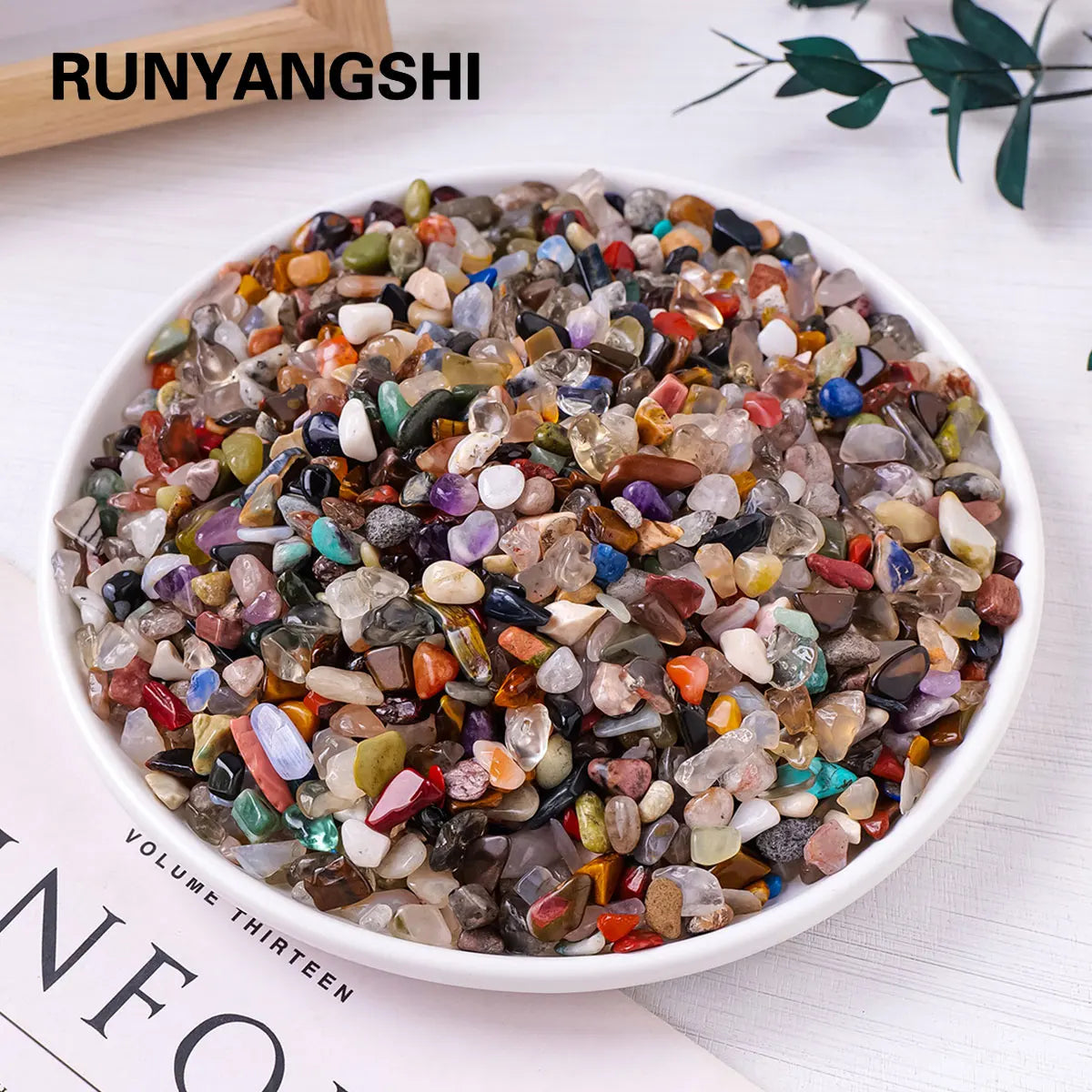 Đĩa đá quý nhỏ nhiều màu sắc gồm đỏ, xanh, tím, vàng, xanh lá, trắng, đặt trên bàn trắng.