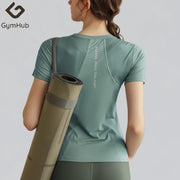 Người mặc áo thể thao xanh lục, mang thảm tập yoga màu nâu, nền xám.