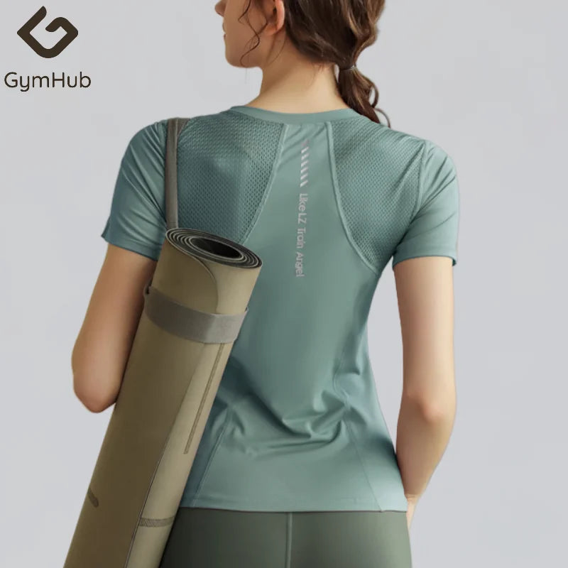 Người mặc áo thể thao xanh lục, mang thảm tập yoga màu nâu, nền xám.
