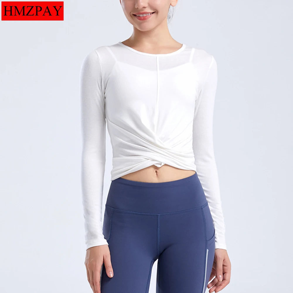 Người mặc áo dài tay trắng xoắn eo và quần legging xanh đậm, nền trắng.