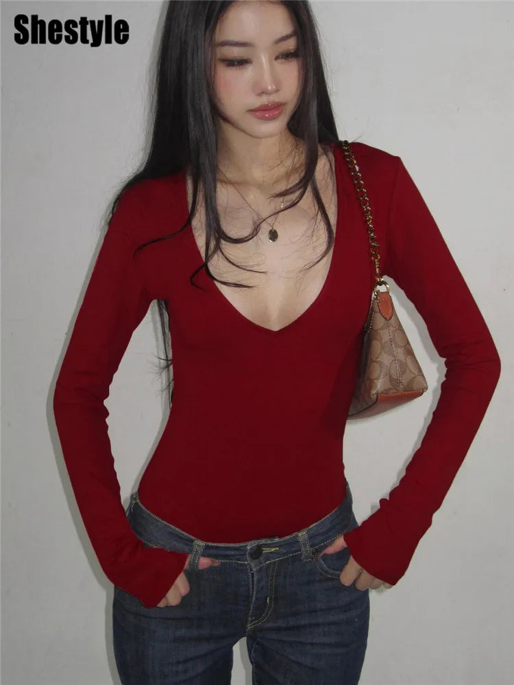 Người mẫu mặc áo đỏ cổ chữ V, tay dài, quần jeans xanh, túi xách màu nâu trên vai.