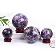 Bốn quả cầu thạch anh tím sáng bóng trên đế gỗ đỏ, nền trắng, có lá cây xanh bên trái.