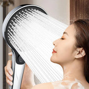 Người phụ nữ nhắm mắt, tận hưởng tia nước từ vòi sen cầm tay, có bọt xà phòng trên vai.