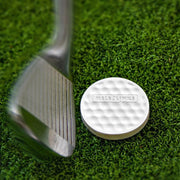 Gậy golf kim loại và đĩa trắng trên cỏ xanh, đĩa có bề mặt lồi lõm.