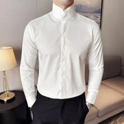 Áo sơ mi trắng cổ cao, tay dài, người mẫu mặc cùng quần đen, phòng có đèn bàn và sofa.