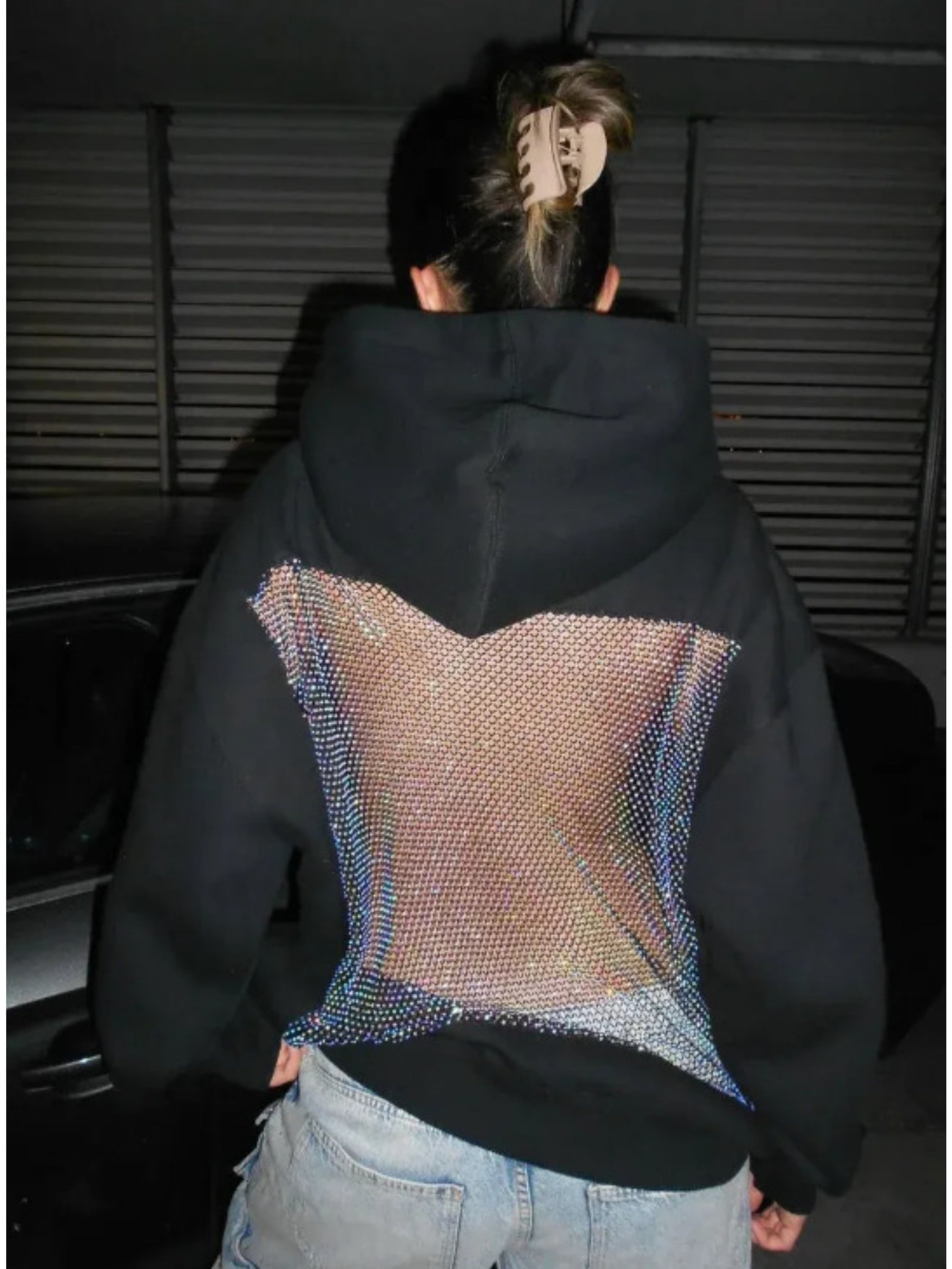 Người mặc áo hoodie đen với phần lưng lưới lấp lánh, tóc búi kẹp càng cua.