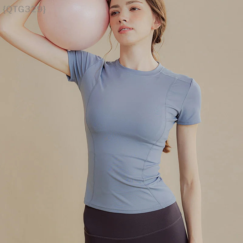 Người phụ nữ mặc áo xanh ôm bóng yoga màu hồng, nền màu be.
