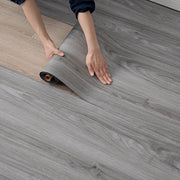 Người đang trải cuộn sàn nhựa vân gỗ màu xám trên nền gỗ sáng.